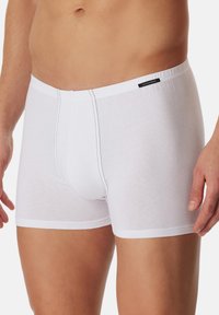 Boxers en coton blancs avec une coupe ajustée, dotés de coutures noires et d'une étiquette logo sur la taille. Texture lisse et longueur mi-cuisse.