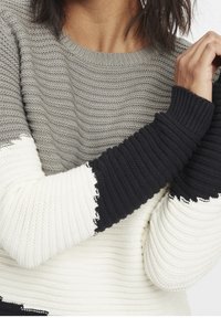 Sweter dzianinowy w odcieniach szarości, bieli i czerni; teksturowany falisty wzór na korpusie; ściągacze z kontrastowymi czarnymi i białymi brzegami.