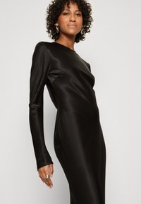 Svart satin langermet kjole med en tettsittende silhuett, glatt tekstur og rund hals, som viser en minimalistisk design.