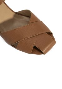 Braune Leder Sandale mit einem Kreuzriemen-Design, offener Zehenpartie und strukturiertem Finish. Verfügt über ein glattes Inneres und einen niedrigen, abgerundeten Absatz.
