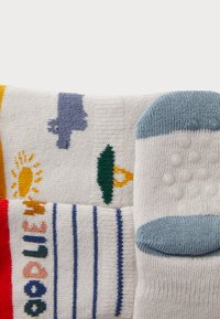 Bunt gemusterte Baumwollsocken: gelbe Sonne, blauer Dinosaurier, grünes Blatt und blaue Grip-Punkte an der Ferse. Weiche Textur, vielfältige Designs.