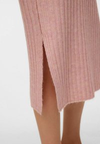 Lang, lyserød ribstrikket nederdel med en sidelæg, der har en blød tekstur og en kant, der let fnulrer, hvilket fremhæver det afslappede look.