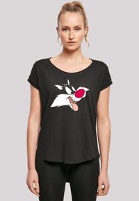 Svart t-skjorte med korte ermer som har et stort grafisk motiv av hodet til en tegneseriefigur med rosa og hvite detaljer. Myk stoffkvalitet med en avslappet passform.