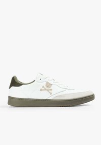 Zapatilla baja blanca con suela y talón verde olivo, logo de calavera y huesos cruzados en beige en el lateral, y cordones blancos.