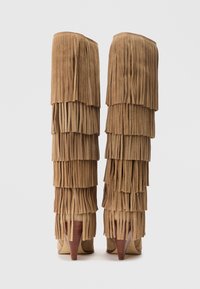 Bottes en daim marron hauteur genou avec des détails de franges superposées, des talons pointus et un bord supérieur lisse. Texturé avec de doux et fluides glands.