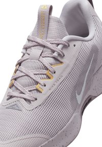 Nike terrengløpesko i lys lilla mesh med teksturert overflate. Har hvit Swoosh, gule aksenter og grå detaljer på sålen.