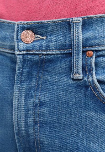 Svijetloplave traperice s metalnim gumbom, prošivenim detaljima i prednjim patentnim zatvaračem. Tkanina ima mekanu teksturu i izblijedjeli finiš.