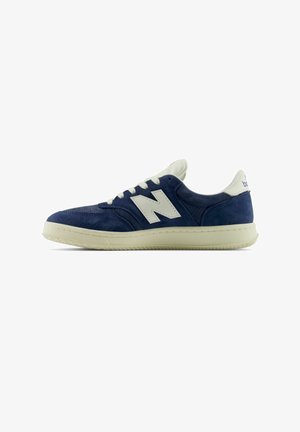 Donkerblauwe suède sneaker met witte leren accenten, voorzien van een opvallend "N"-logo, ronde neus, platte rubberen zool en veterluiting.