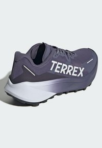 Zapatilla de running morada con parte superior de malla, marca "TERREX" en blanco, suela acolchada y suela exterior texturizada en negro para tracción.