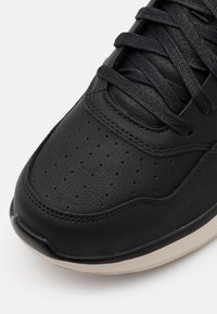 Czarne skórzane sneakersy z perforowanym noskiem, płaskimi czarnymi sznurowadłami i jasną gumową podeszwą. Posiadają zaokrąglone krawędzie i gładką fakturę.