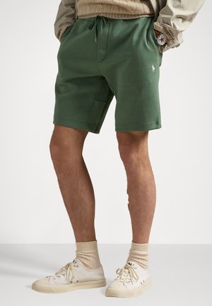 Shorts en mélange de coton vert avec une taille élastique, un cordon de serrage et des poches latérales. Associés à des baskets blanches et des chaussettes crème.