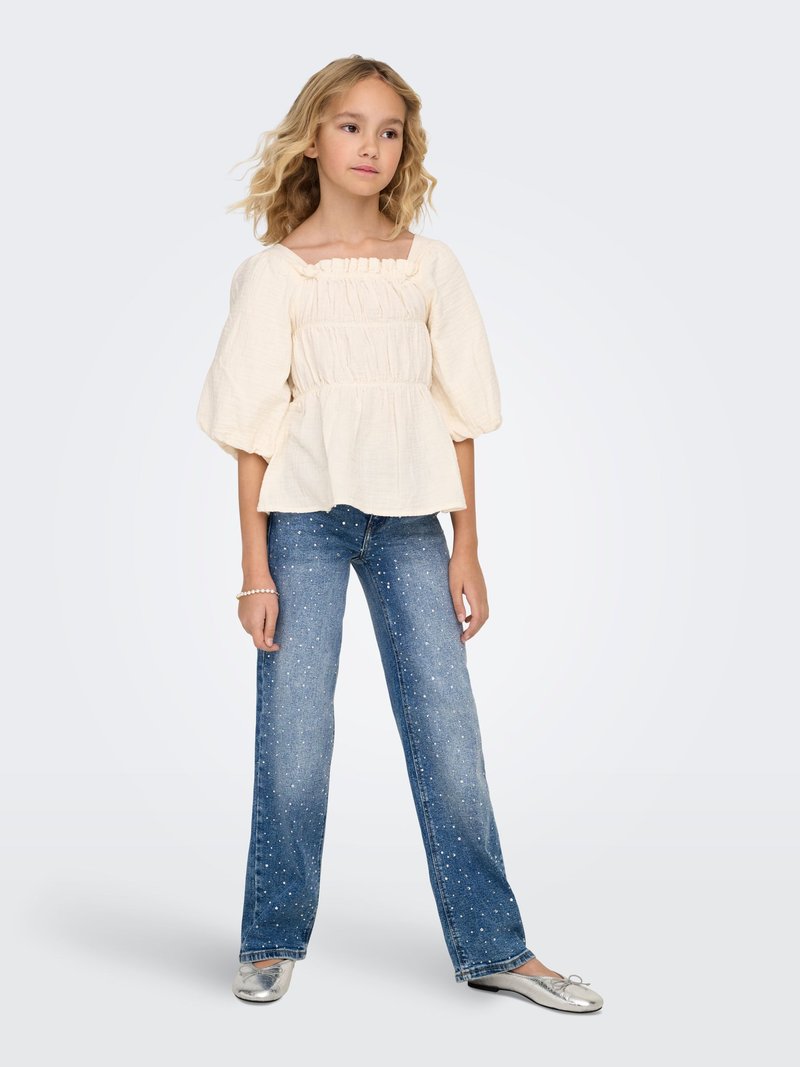 Lauku stila blūze gaiši krēmā ar volānu apkakli un pūkainām piedurknēm. Kombinēta ar ziliem džinsa biksēm ar baltām plankām un sudraba krāsas dzīvokļiem.