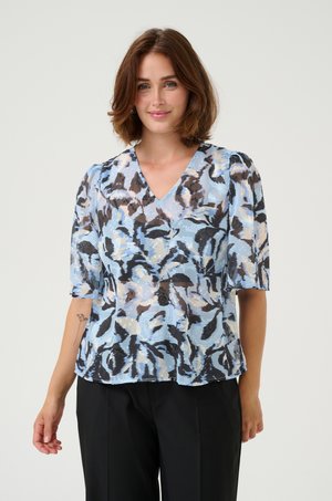 Light blue blouse with abstract black and taupe patterns, V-neckline, and short puff sleeves, made from a semi-sheer fabric.