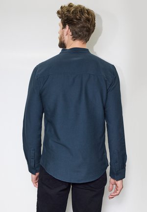 Camicia a maniche lunghe blu scuro realizzata in tessuto testurizzato, con colletto a punta e polsini abbottonati, mostrata da dietro.