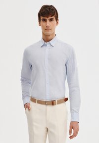 Jasnoniebieska koszula z długim rękawem i kołnierzykiem zapinanym na guziki, wykonana z miękkiego materiału, w połączeniu z kremowymi spodniami i beżowym plecionym pasem.