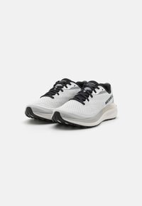 Zapatillas deportivas blancas con una parte superior de malla transpirable, cordones negros y una suela texturizada. En el costado presenta la marca "MERRELL" en gris.