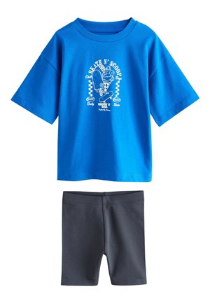 Blå T-shirt med korte ærmer med hvidt skateboardmotiv og tekst, kombineret med ensfarvede mørkegrå knælange shorts.
