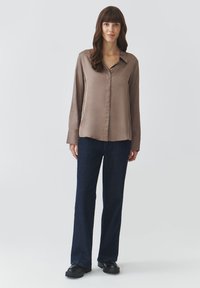 Long-sleeve, light brown satin shirt with a button-down front, paired with dark navy wide-leg jeans and black platform shoes.
