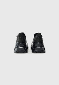 Chaussures de sport noires avec un tige en tricot texturé, col rembourré et accents réfléchissants. Semelle en caoutchouc noire épaisse avec un motif de bande de roulement prononcé.