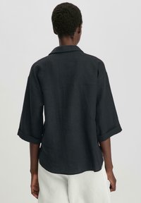 Camicia in lino grigio scuro con vestibilità comoda, maniche a risvolto e colletto. La parte posteriore presenta un design semplice senza motivi.