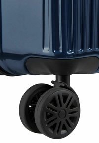 Angolo di una valigia rigida blu navy con ruote in gomma nera caratterizzate da un design a raggi, superficie texturizzata e scanalature verticali.