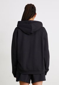 Juodas džemperis su gobtuvu, pagamintas iš minkštos medžiagos. Turi laisvą siluetą ir įpjautą apykaklę. Derinamas su atitinkančiomis šortais, kad sukurtų šiuolaikinį įvaizdį.