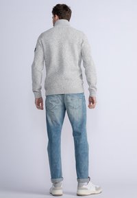 Harmaa ribbikuvioinen villapaita, jossa on korkea kaulus, teksturoitu neulekuvio ja pitkät hihat, yhdistettynä vaaleansinisiin farkkuihin ja valkoisiin lenkkareihin.