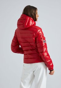 Rode gewatteerde jas met een glanzende afwerking, voorzien van een capuchon, elastische boorden en een patchdetail op de linkermouw. Gestreept stikpatroon zichtbaar.