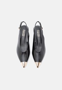 Escarpins noirs en simili cuir avec une belle pointe, dotés d'un accent métallique doré à l'extrémité. Texture lisse, design élégant.