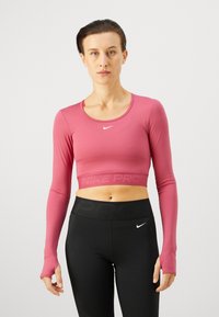Rozā garo piedurknu sporta tops, ar apaļu kakla izgriezumu un caurumiem īkšķiem. Apakšmalā ir tekstūrēta "NIKE PRO" lente.