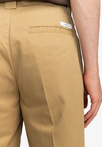 Khaki trousers with a smooth, matte texture, featuring a back pocket and a small label tag. The design is straight-cut and tailored.