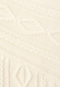 Kremfarvet strikket stof med teksturerede mønstre, herunder snoninger og diamanter, der skaber et blødt, hyggeligt udseende.