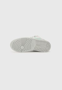 Semelle blanche de basket avec des motifs circulaires et rectangulaires, montrant le logo Nike au centre sur un fond clair uni.
