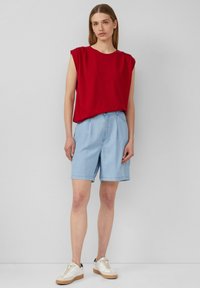 Rood T-shirt met korte mouwen, gecombineerd met lichtblauwe shorts. De outfit heeft een ontspannen pasvorm, zachte stof en klassieke sneakers in wit en beige.