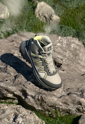 Chaussure de randonnée grise avec un design texturé, tige en mesh, semelle en caoutchouc et accents verts. Présente un embout renforcé et un col rembourré.
