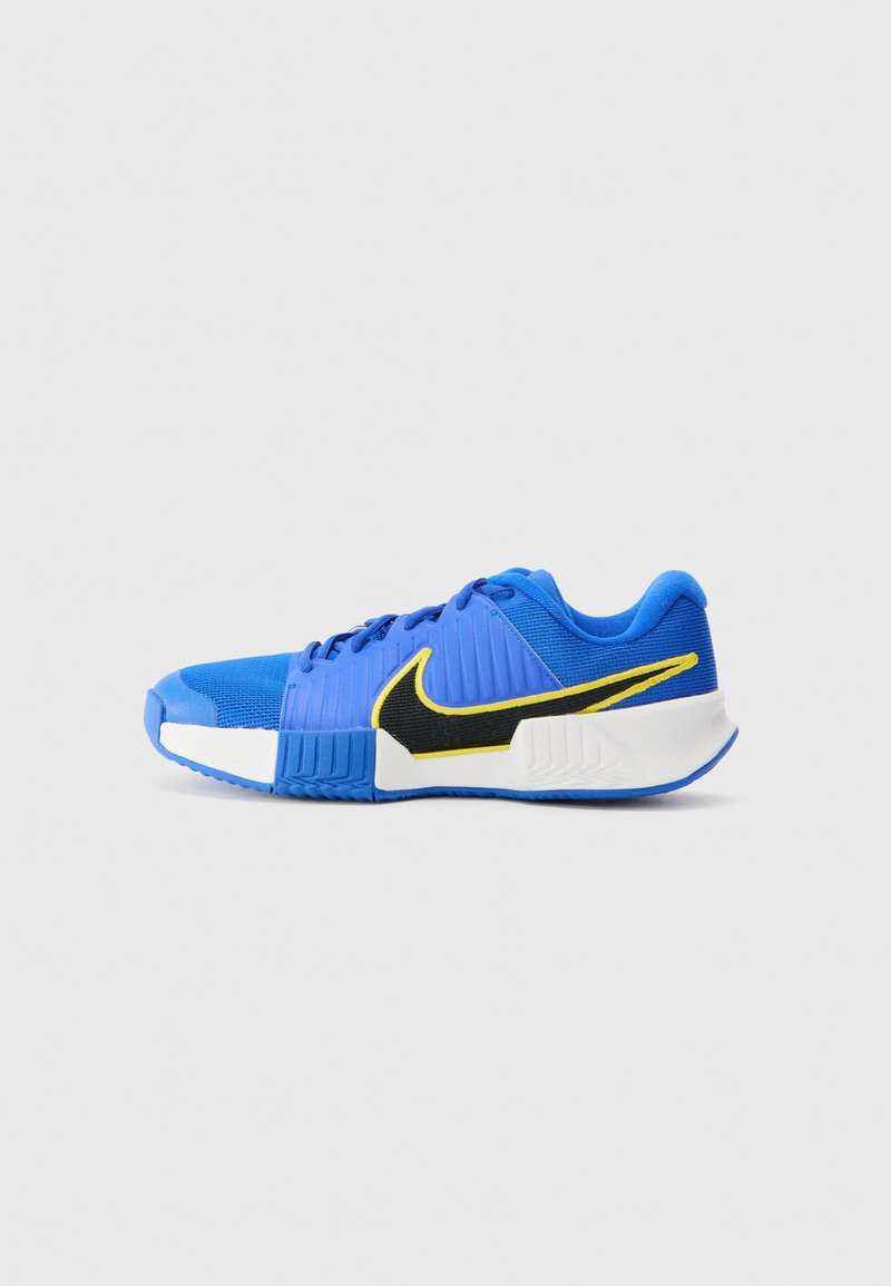 Blå atletisk sko med teksturert overdel, med en svart Nike-swoosh og gule detaljer. Hvit mellomsåle og blå yttersåle fullfører designet.