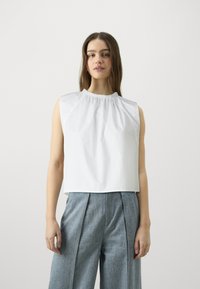 Top bianco senza maniche con scollo arricciato, realizzato in tessuto liscio; abbinato a pantaloni a palazzo larghi di colore azzurro chiaro con texture.