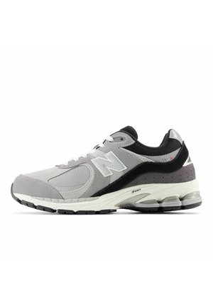 Baskets de sport grises, noires et blanches en mesh et daim, lacets blancs, semelle rembourrée et logo "N" sur le côté.