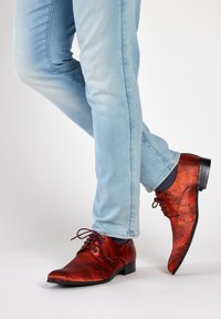 Rode leren dresschoenen met een patroon en een spitse neus, gecombineerd met lichtblauwe slim-fit jeans. Donkere zool en bijpassende veters.