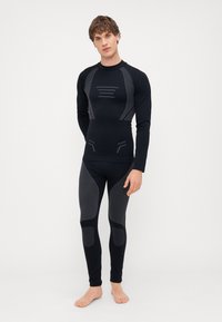 Zwart sportief basislaagset met een lang mouwtop en strakke leggings met textuur in grijs en geometrische patronen.