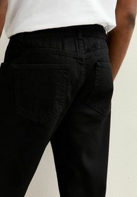 Jeans de mezclilla negra con un corte relajado, que cuentan con dos bolsillos traseros, líneas limpias y una textura sutil. Sin logotipos ni adornos visibles.