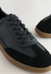 Zapatillas de cuero negro y ante con cordones planos, una parte superior texturizada y suelas de goma. Presentan una puntera suave y acentos en contraste.