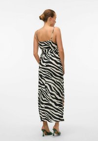 Robe maxi avec un motif zèbre noir et blanc, des bretelles spaghetti ajustables et des fentes sur les côtés. Associée à des chaussures à talons hauts vertes.