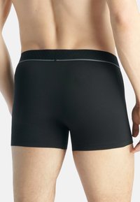 Svarta boxerkalsonger med en åtsittande design, mjukt material och en subtil texturerad midjeband. Har en halvhög skärning och släta sömmar.