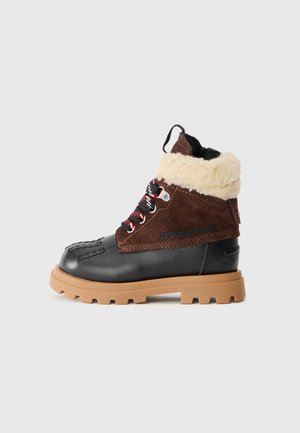 Bottine marron et noire avec une tige en daim, un bord en fourrure, des lacets noirs et une semelle en caoutchouc épaisse avec un motif de crampons.