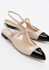 Bailarinas de piel beige con parte delantera de charol negro en punta, con una correa con hebilla metálica y tacón plano.