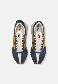 Zapatillas de ante en azul marino y amarillo con un diseño texturizado. Presentan cordones blancos, una lengüeta acolchada y una suela de goma negra.