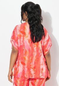 Top corto a maniche corte, dal taglio ampio, in un vivace motivo tie-dye nei toni del rosa e dell'arancione. Tessuto leggero con una texture liscia, presenta fessure laterali.
