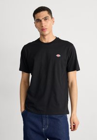 Black cotton t-shirt featuring a crew neckline and short sleeves, with a small multicolored logo on the chest and straight hem.