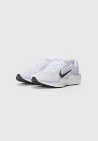 Hvite treningssko med overdel i mesh, med en svart Nike Swoosh, lilla detaljer på hælen, og en strukturert svart yttersåle.